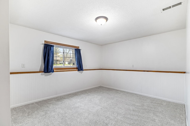 spare room featuring a textured ceiling, visible vents, baseboards, and carpet