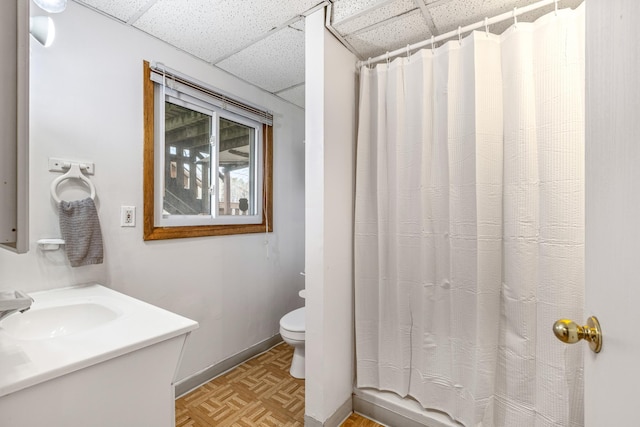 bathroom featuring baseboards, a drop ceiling, toilet, and curtained shower