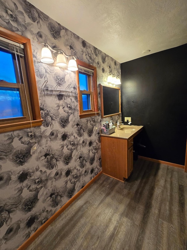 1014 3rd Ave SW, Pipestone, MN 56164 - bathroom with vanity, baseboards, wallpapered walls, a textured ceiling, and wood finished floors
