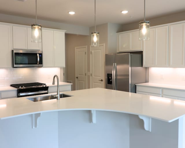 kitchen featuring a breakfast bar, light countertops, a sink, stainless steel appliances, and backsplash