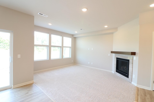 unfurnished living room with visible vents, a wealth of natural light, a glass covered fireplace, and baseboards
