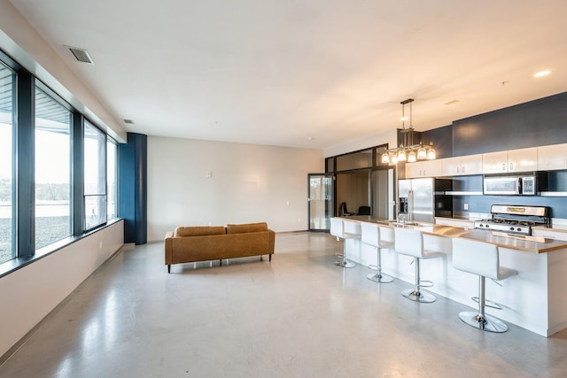 kitchen with stainless steel appliances, a breakfast bar, visible vents, pendant lighting, and finished concrete floors