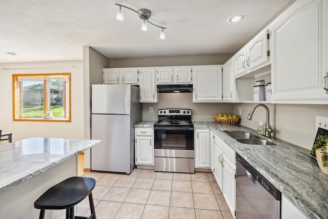 kitchen with appliances with stainless steel finishes, a sink, under cabinet range hood, light stone counters, and a textured ceiling