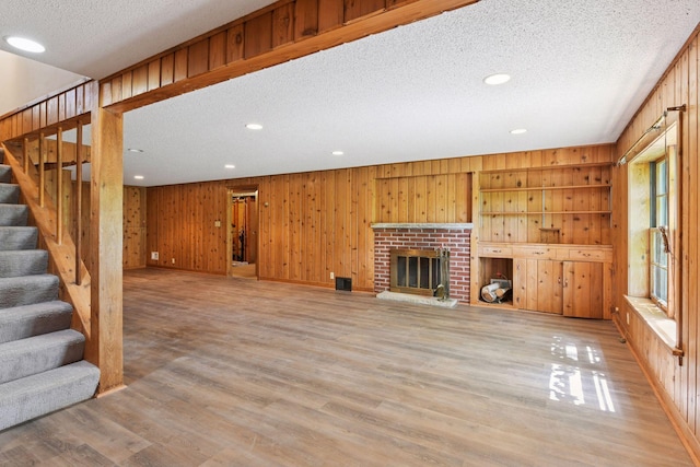 9017 31st St, Saint Louis Park, MN 55426 - unfurnished living room with a textured ceiling, stairs, light wood finished floors, wood walls, and a brick fireplace