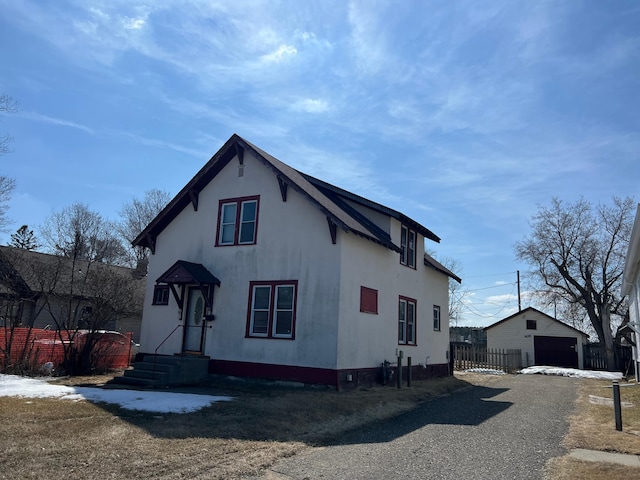 view of front facade featuring a garage, stucco siding, an outdoor structure, and fence