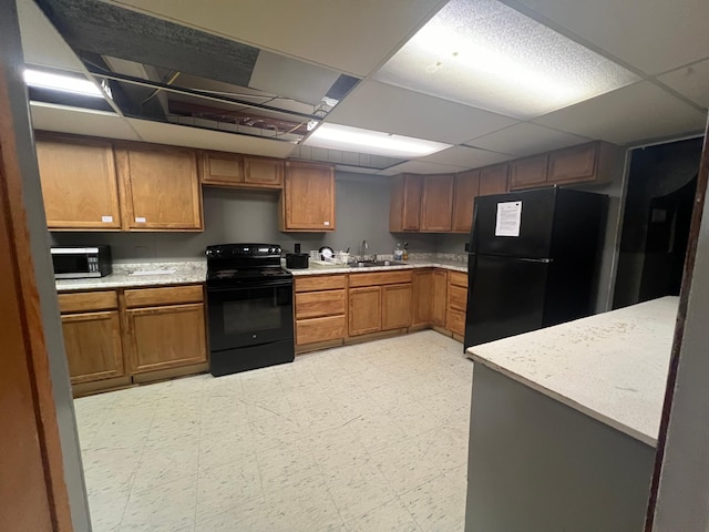 kitchen with light countertops, brown cabinetry, black appliances, a drop ceiling, and light floors