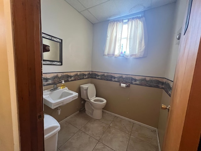 half bathroom featuring toilet, tile patterned floors, a sink, and a drop ceiling