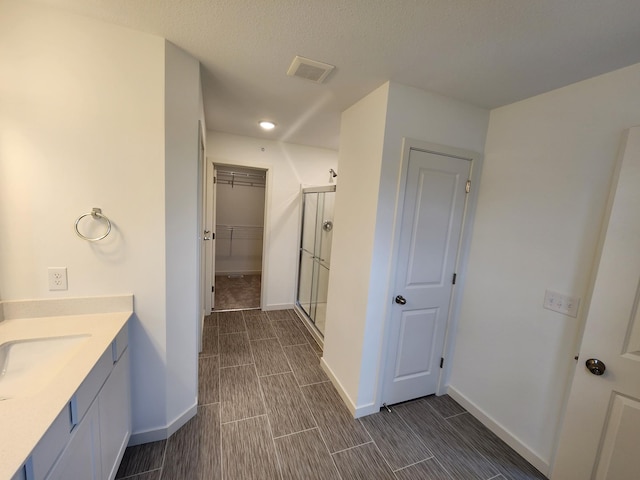 full bath with visible vents, baseboards, a walk in closet, a shower stall, and vanity