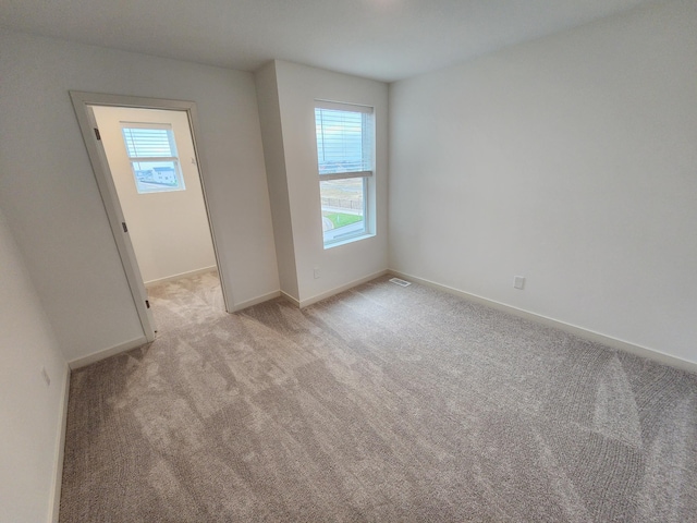spare room featuring visible vents, light colored carpet, baseboards, and plenty of natural light
