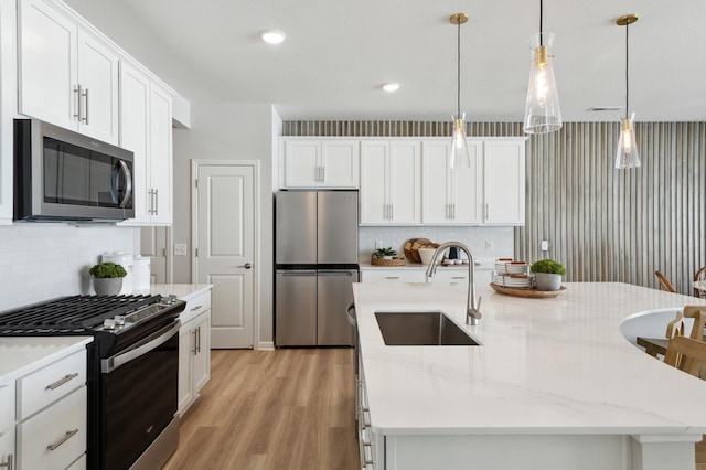 kitchen featuring an island with sink, light wood-style flooring, a sink, stainless steel appliances, and decorative backsplash