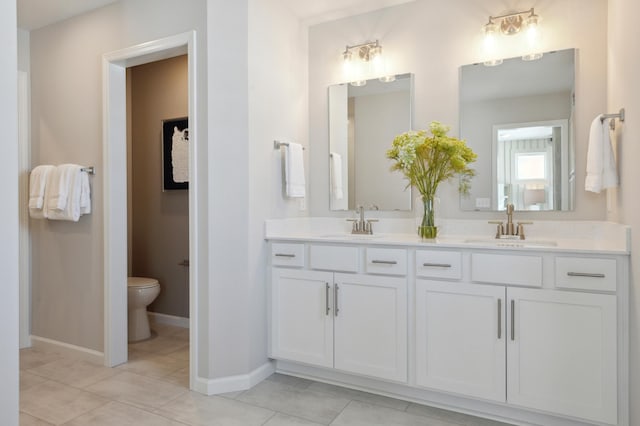 bathroom featuring toilet, double vanity, a sink, and baseboards