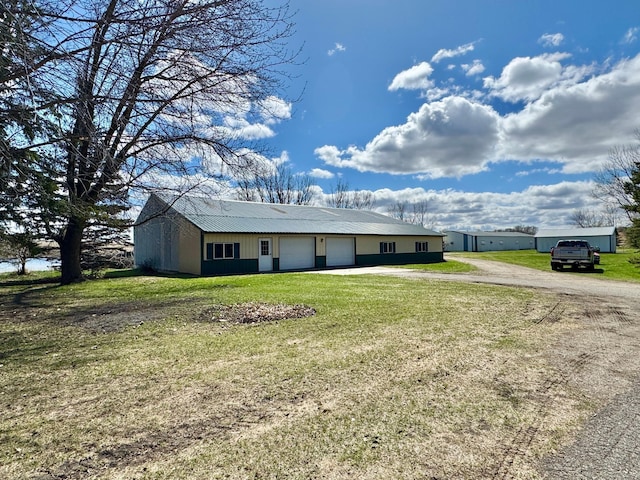 single story home featuring a detached garage, a front yard, metal roof, and driveway