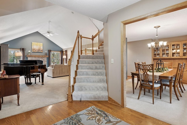 interior space featuring wood finished floors, stairs, vaulted ceiling, ceiling fan with notable chandelier, and a brick fireplace
