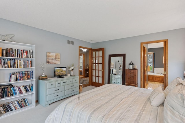 bedroom with light colored carpet, visible vents, french doors, and ensuite bath