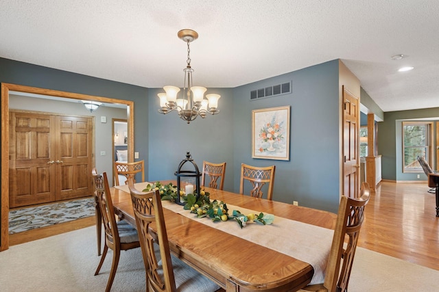 dining area featuring light wood-style flooring, light colored carpet, visible vents, a notable chandelier, and a textured ceiling