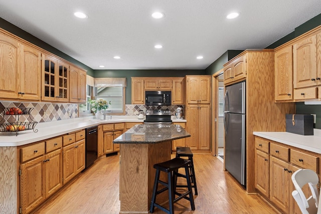 kitchen with black appliances, light wood finished floors, a sink, and a breakfast bar