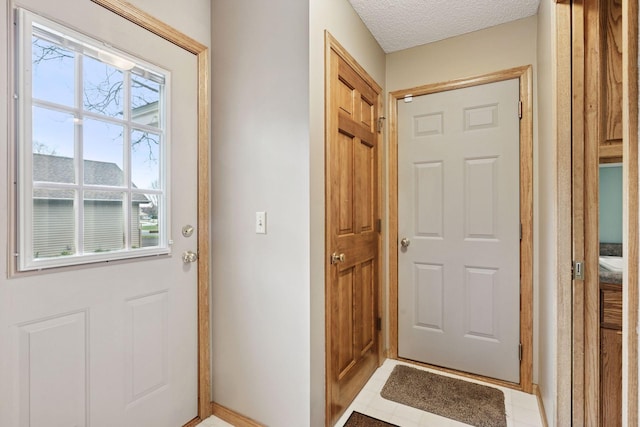doorway featuring a wealth of natural light, light tile patterned floors, a textured ceiling, and baseboards