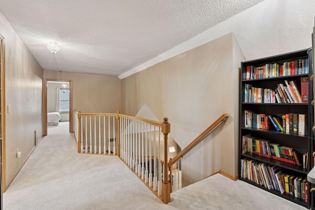 hallway with an upstairs landing, carpet flooring, and a textured ceiling