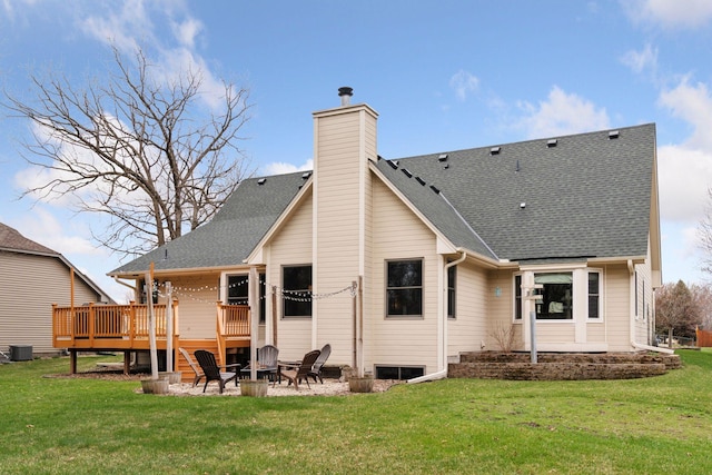 back of property with a deck, a chimney, roof with shingles, an outdoor fire pit, and a lawn