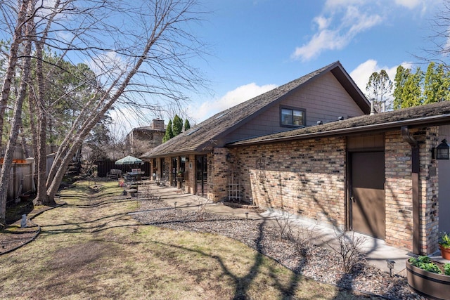 view of property exterior with fence, brick siding, a chimney, and a shingled roof