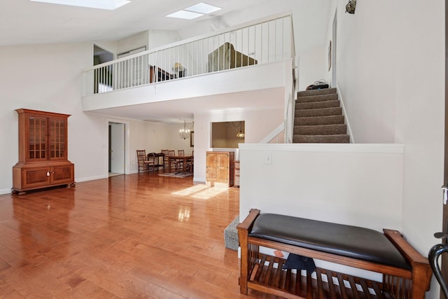 stairs with wood finished floors, a towering ceiling, a skylight, a chandelier, and baseboards