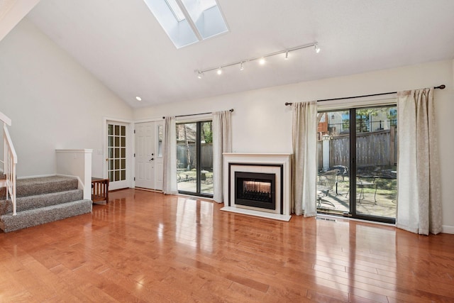 unfurnished living room with wood finished floors, a skylight, stairway, a fireplace, and high vaulted ceiling