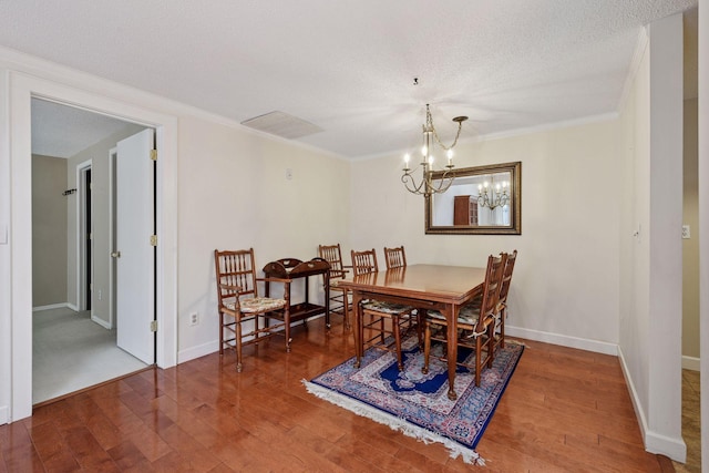 dining room featuring wood finished floors, a chandelier, baseboards, crown molding, and a textured ceiling
