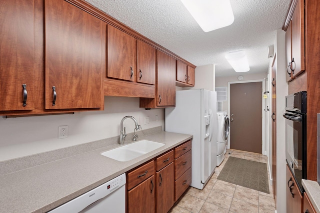 kitchen featuring independent washer and dryer, a sink, a textured ceiling, white appliances, and light countertops