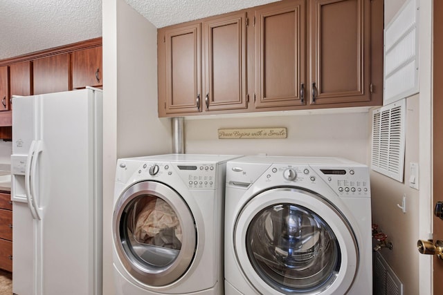 clothes washing area featuring separate washer and dryer, a textured ceiling, and cabinet space