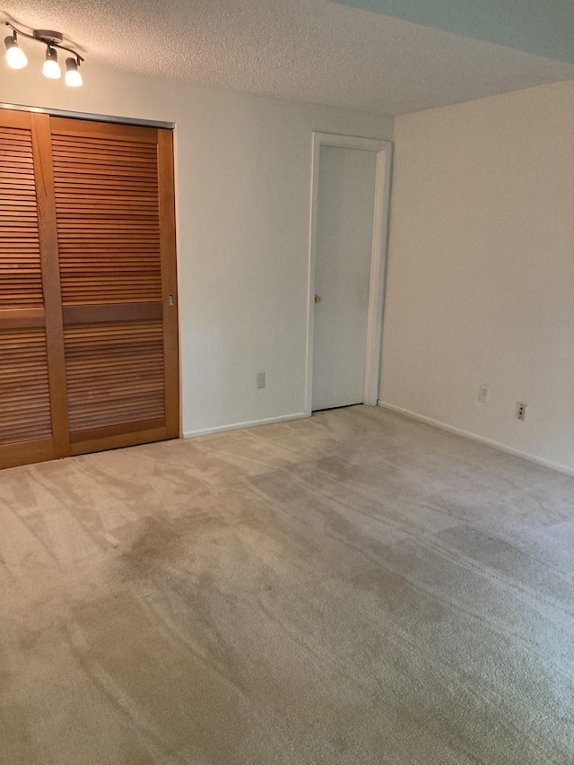 carpeted empty room with a textured ceiling and baseboards