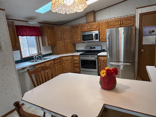 54966 Rainbow Rd, Sand Lake Twp, MN 56636 - kitchen featuring appliances with stainless steel finishes, wallpapered walls, vaulted ceiling, a skylight, and brown cabinets