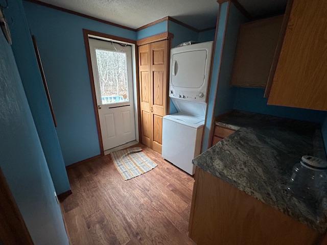 54966 Rainbow Rd, Sand Lake Twp, MN 56636 - laundry room featuring stacked washer / dryer, light wood-type flooring, a textured ceiling, and crown molding
