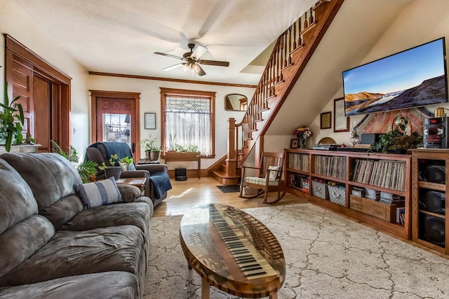 living area with ornamental molding, ceiling fan, stairway, and wood finished floors