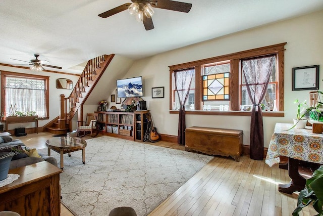 living area with a ceiling fan, baseboards, stairs, and a healthy amount of sunlight