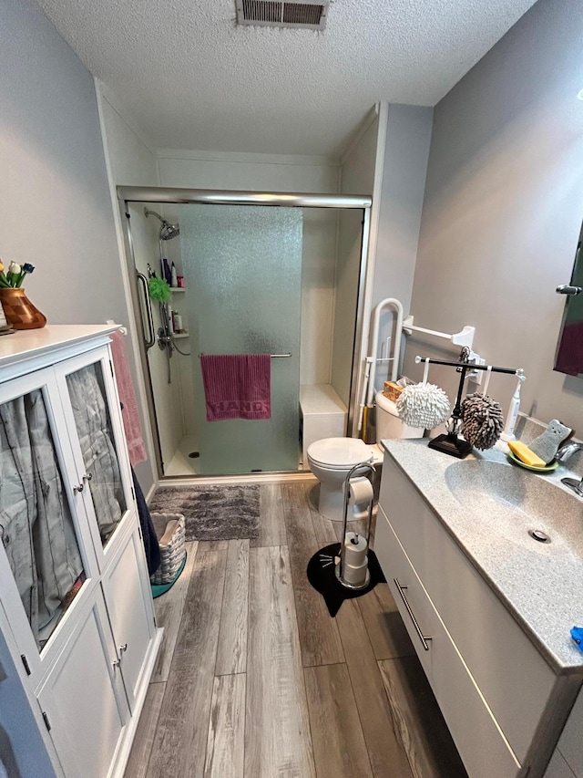 2548 Sumac Rdg, White Bear Lake, MN 55110 - bathroom featuring visible vents, wood finished floors, toilet, a textured ceiling, and a shower stall