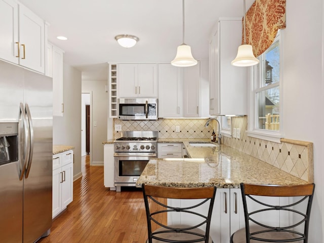 kitchen featuring stainless steel appliances, a sink, light wood-type flooring, white cabinets, and a peninsula