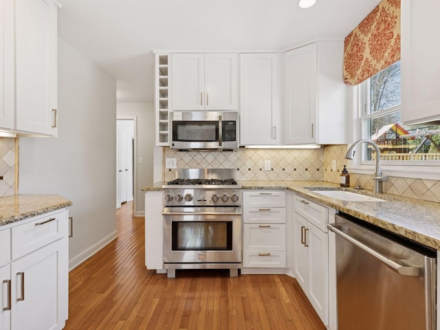 kitchen featuring stainless steel appliances, a sink, open shelves, light wood-type flooring, and white cabinetry