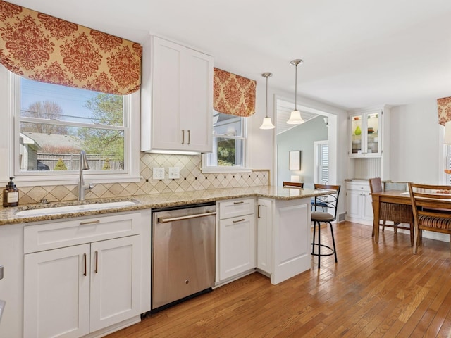 kitchen with dishwasher, a sink, light wood-style floors, white cabinetry, and tasteful backsplash