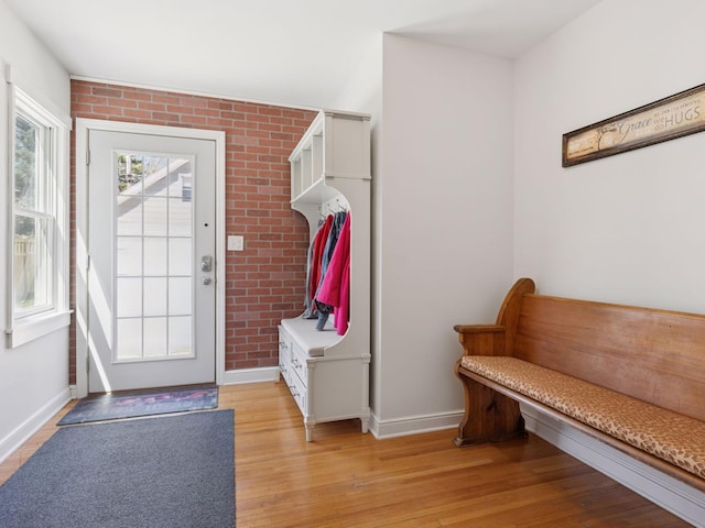 mudroom featuring baseboards, light wood finished floors, and brick wall
