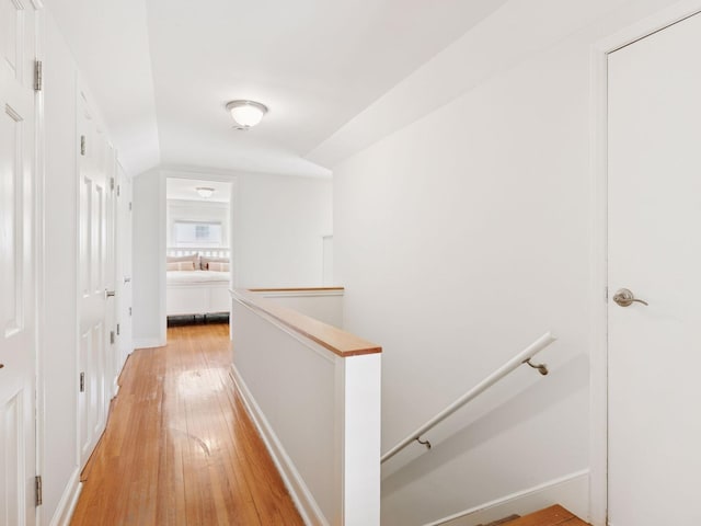 hallway featuring an upstairs landing, light wood finished floors, lofted ceiling, and baseboards