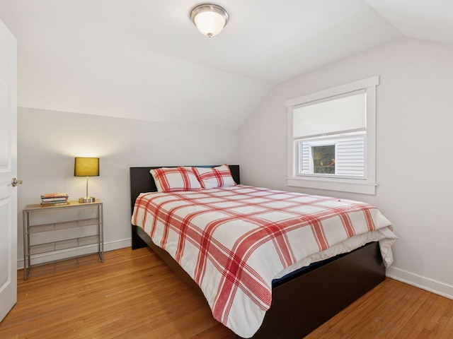 bedroom with vaulted ceiling, wood finished floors, and baseboards