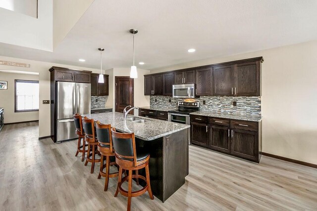 1408 72nd Ave S, Fargo, ND 58104 - kitchen with stainless steel appliances, a sink, decorative backsplash, dark brown cabinets, and light stone counters