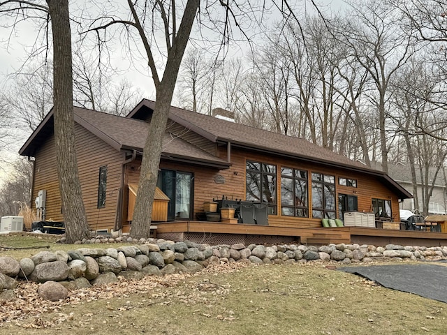 rear view of house with roof with shingles, a wooden deck, a chimney, and central AC