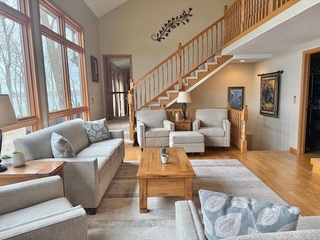 living room with stairway, high vaulted ceiling, and wood finished floors