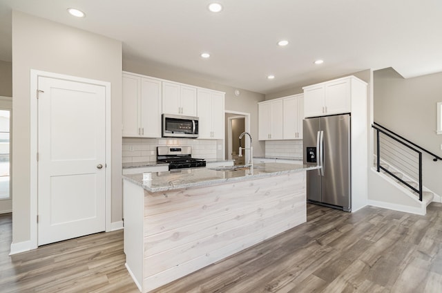 kitchen with decorative backsplash, light wood finished floors, stainless steel appliances, and a sink