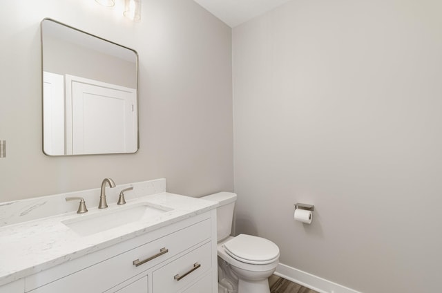 half bath with baseboards, wood finished floors, toilet, and vanity