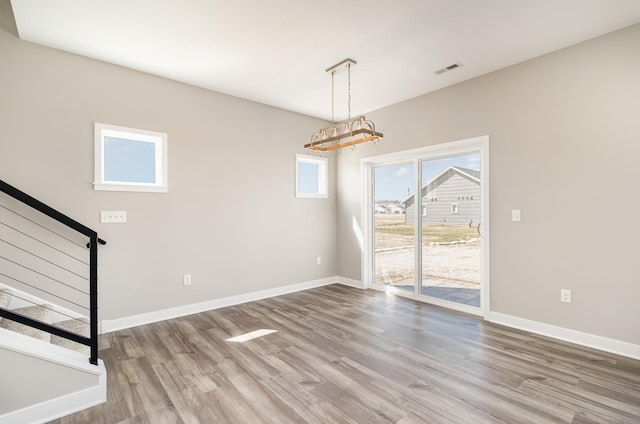 unfurnished dining area featuring stairway, an inviting chandelier, wood finished floors, visible vents, and baseboards