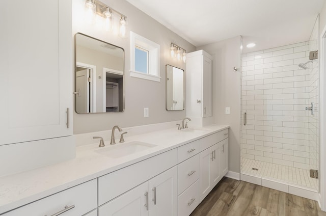 bathroom with wood finished floors, a sink, double vanity, and a stall shower