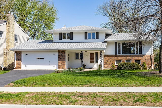 split level home with an attached garage, a front yard, brick siding, driveway, and a shingled roof
