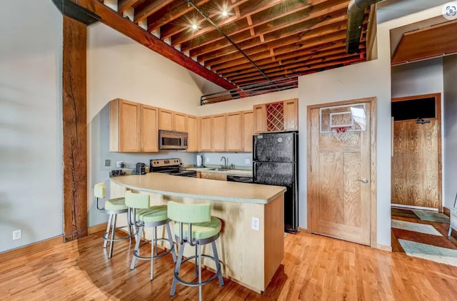 kitchen with a breakfast bar, light countertops, a sink, stainless steel appliances, and light brown cabinets